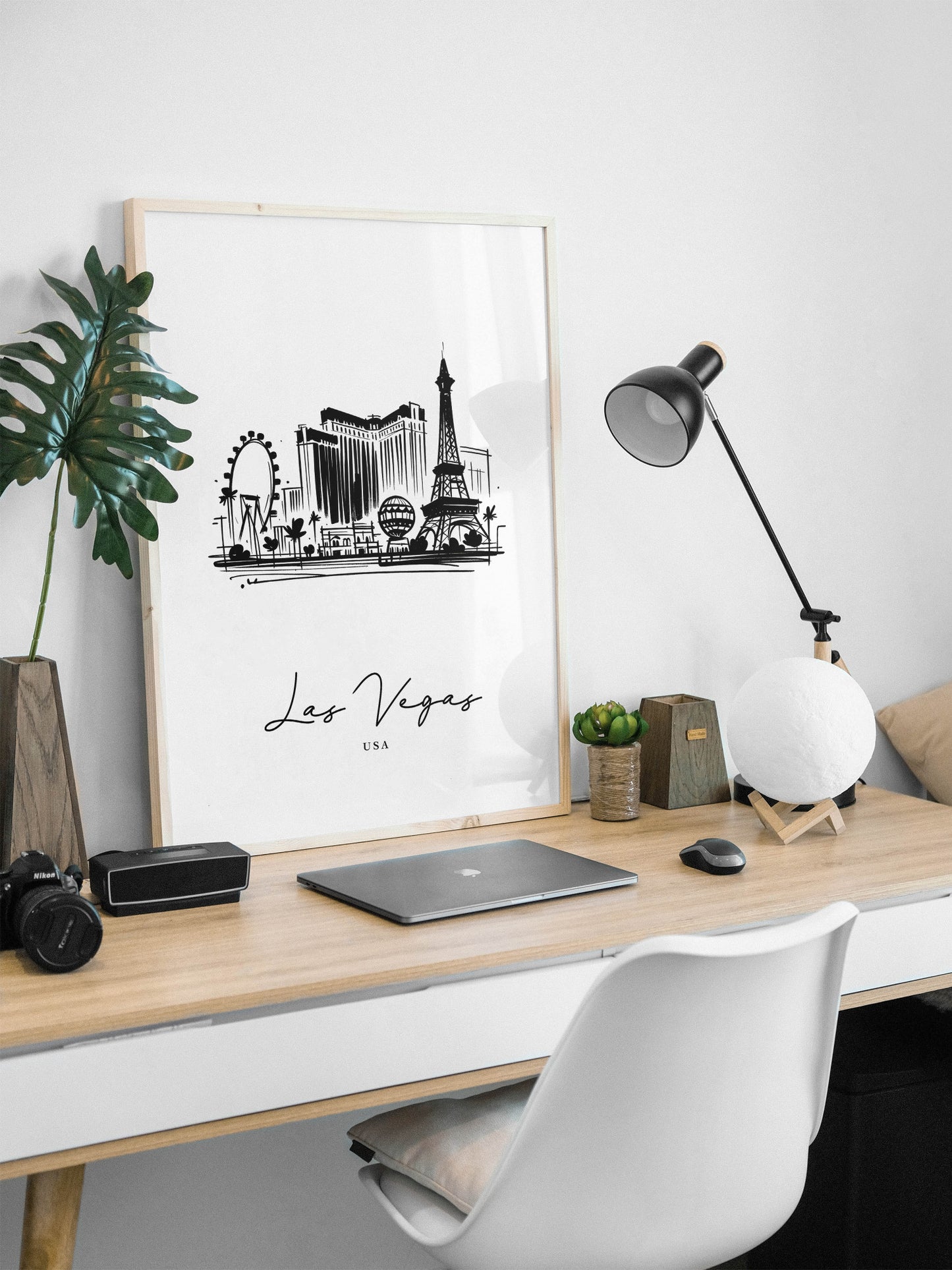 Poster des monuments de Las Vegas en cadre bois clair posé sur un bureau, lampe noire et ordinateur portable