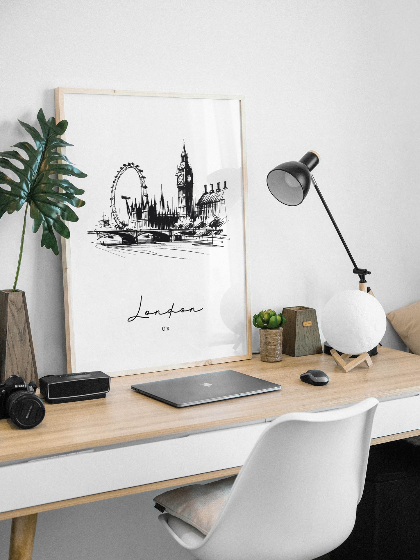 Poster Londres noir et blanc en cadre bois clair posé sur un bureau, lampe noire et ordinateur portable