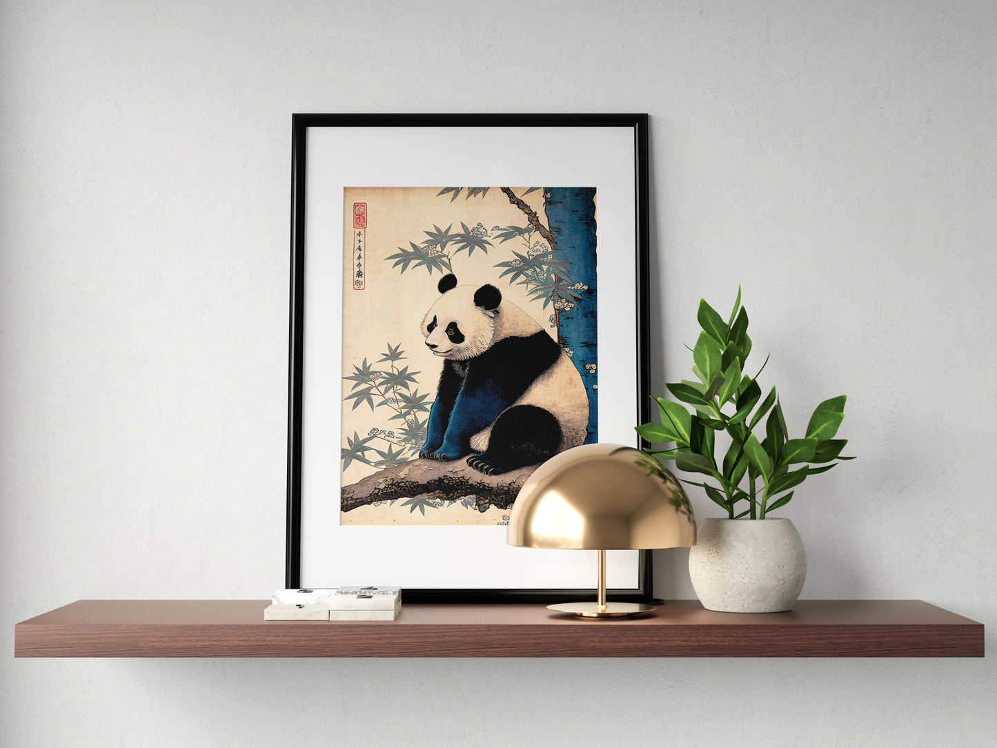 Japanese art panda poster in a black frame with mat on a shelf with a gold lamp and plant