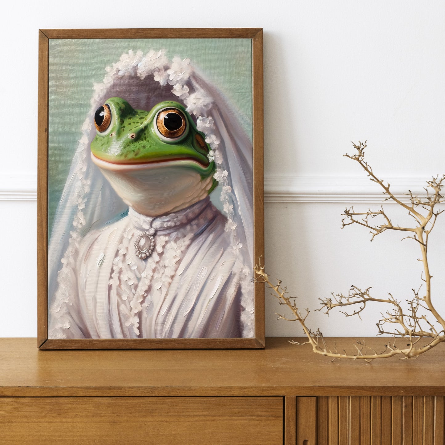 Frog in wedding dress poster in a dark wood frame on a wooden sideboard with a decorative branch