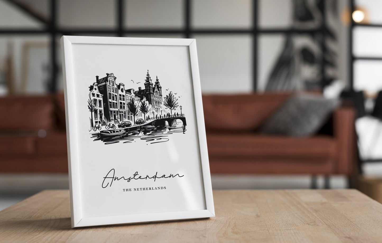 Poster des canaux d'Amsterdam dans un cadre blanc posé sur une table en bois, salon avec canapé en cuir