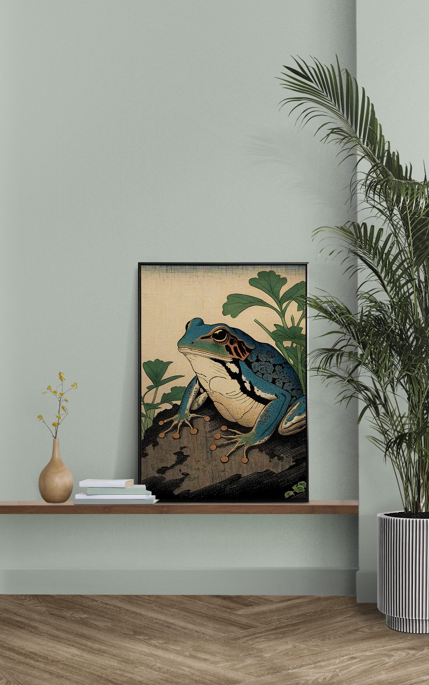 Poster grenouille art japonais posé sur une étagère murale, mur vert sauge et palmier en pot