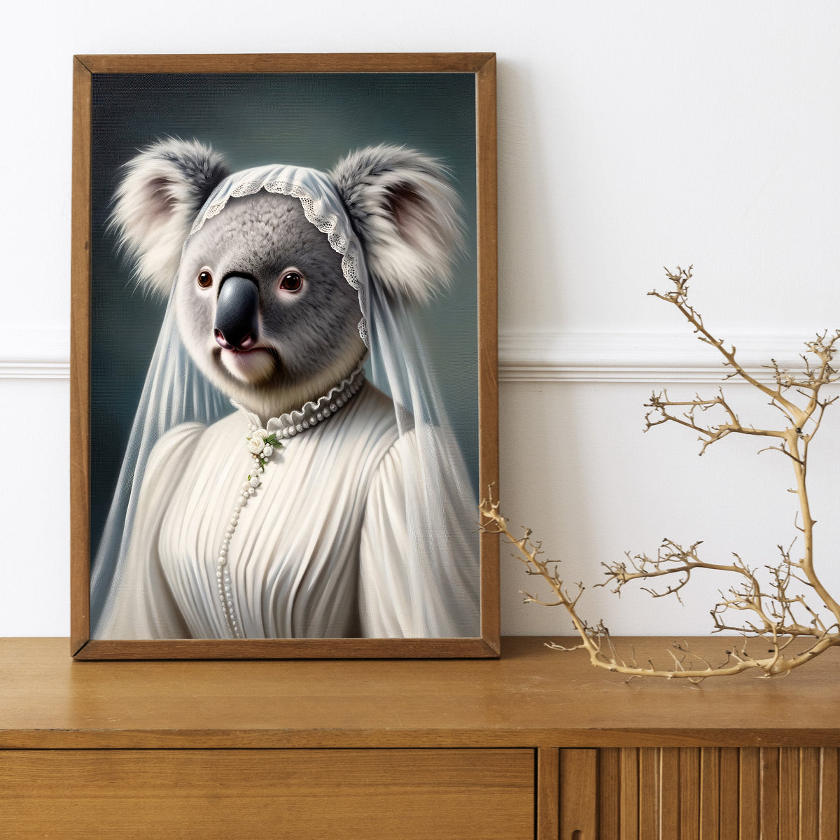 Koala in wedding dress poster in a dark wood frame on a wooden sideboard with a decorative branch