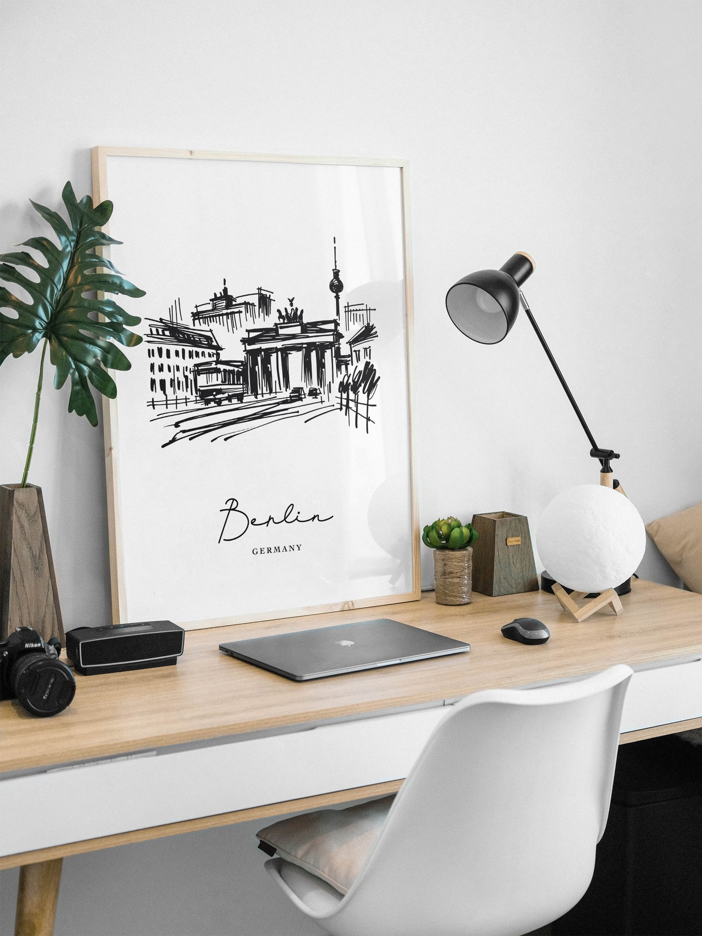 Black and white Berlin poster, natural wood frame on a white desk with an architect lamp and plant