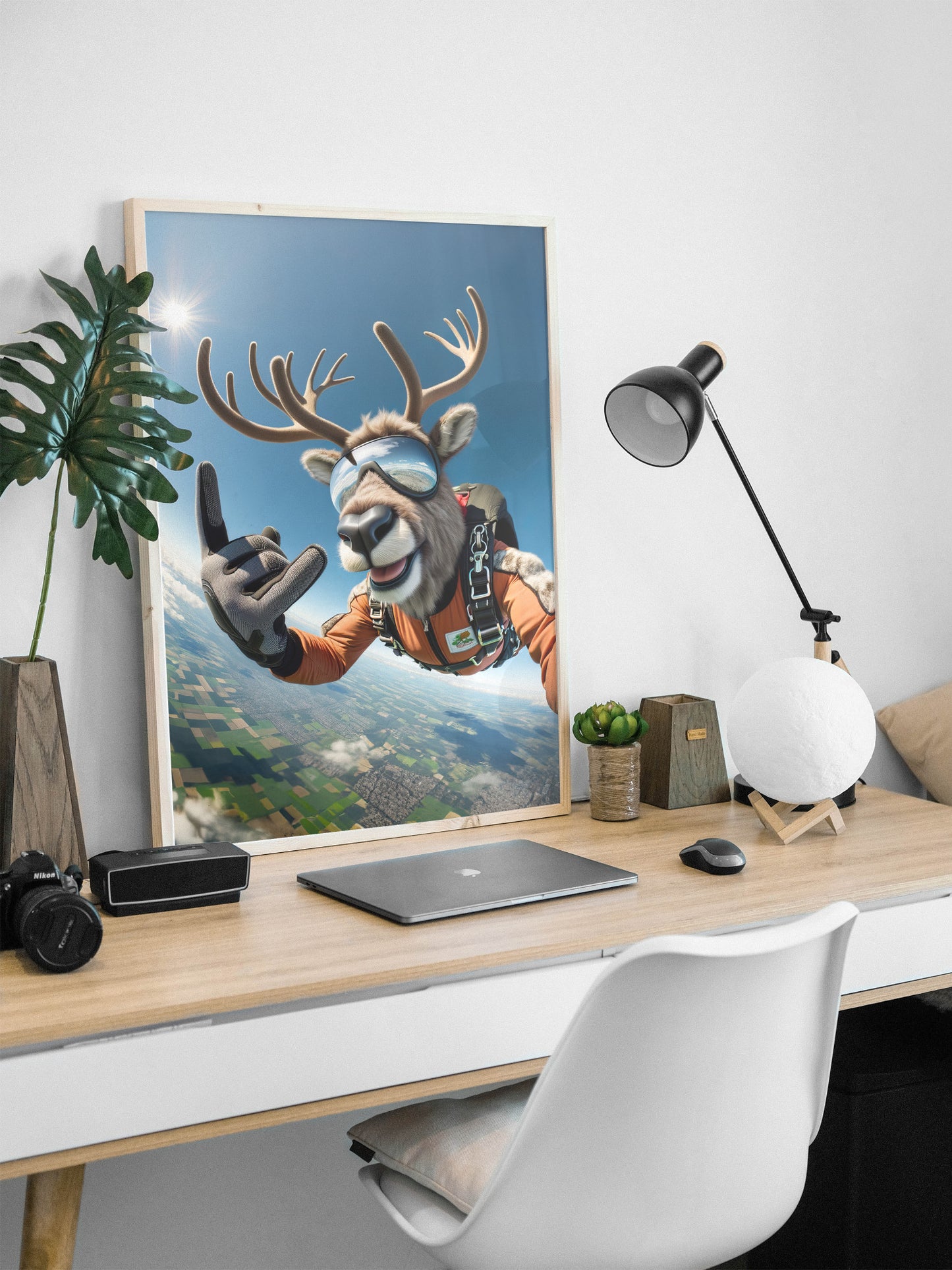 Skydiver caribou poster in a natural wood frame on a desk with a plant and desk lamp