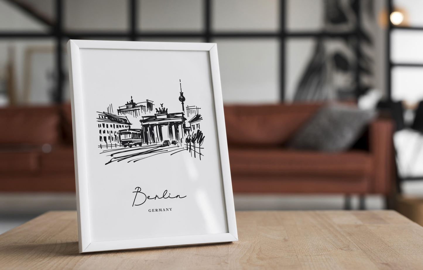 White-framed black and white Berlin poster standing on a wooden table in front of a leather couch