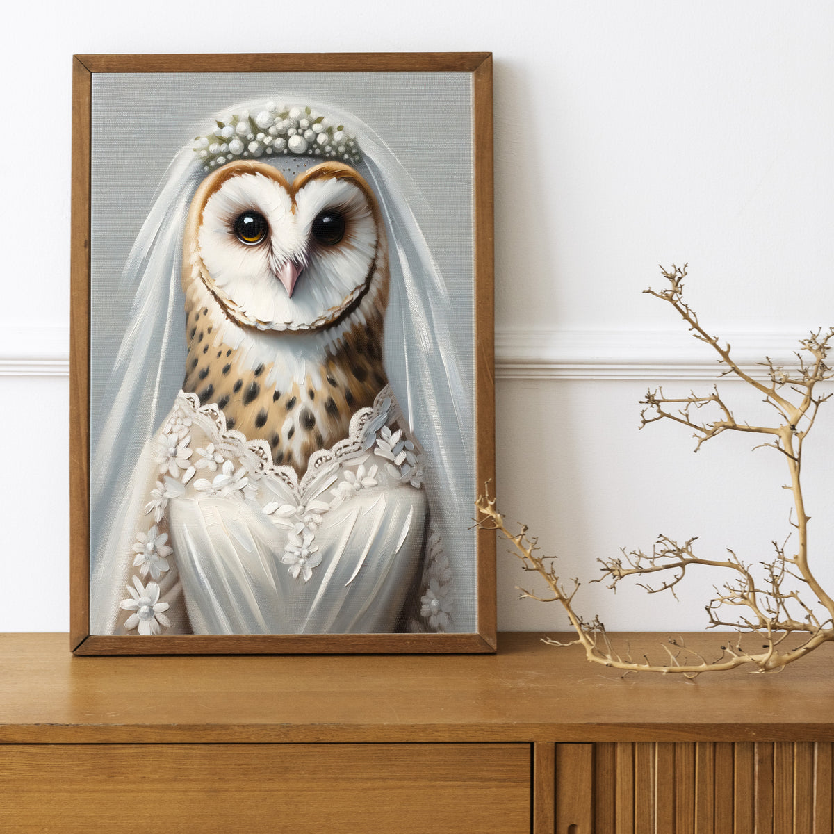 Poster chouette en robe de mariée, cadre bois foncé sur un buffet en bois avec une branche décorative