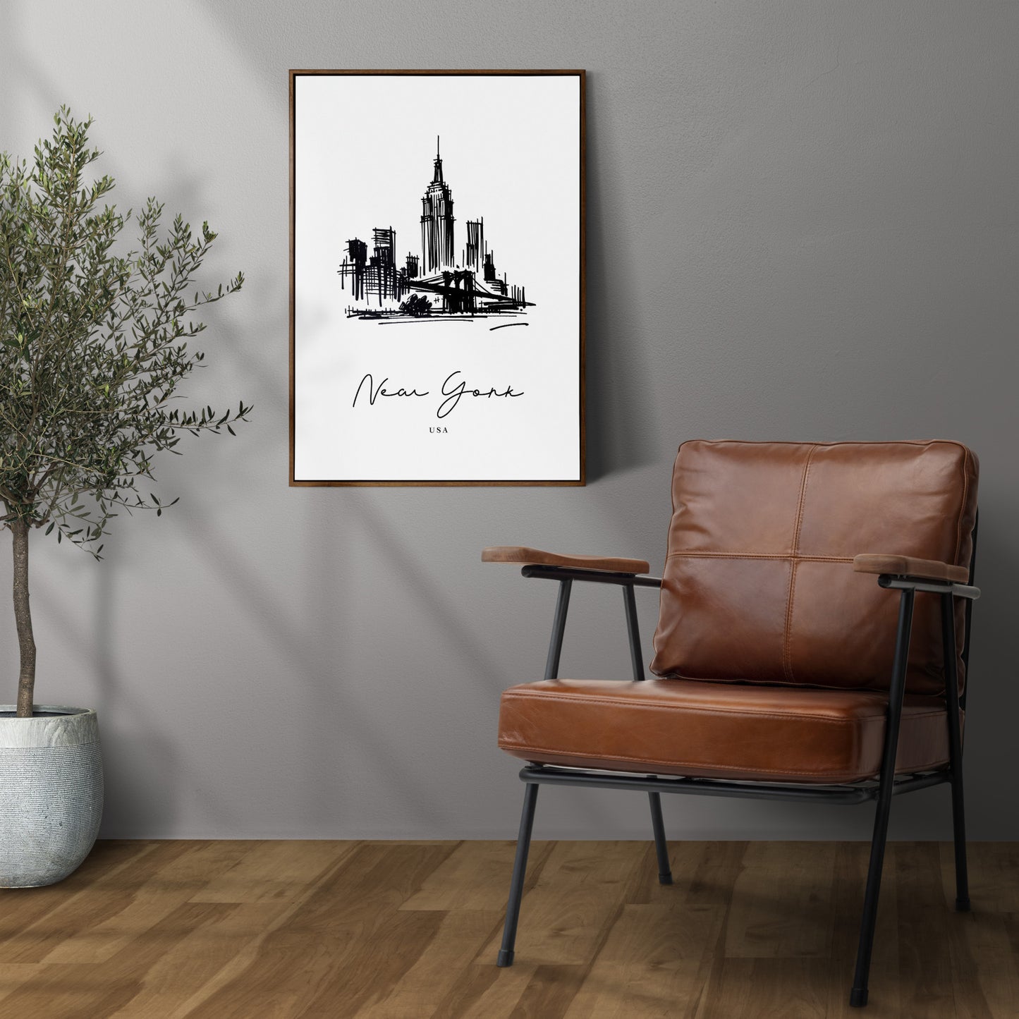 Poster paysage New York en cadre bois foncé sur un mur gris, à côté d'un fauteuil en cuir et d'un olivier