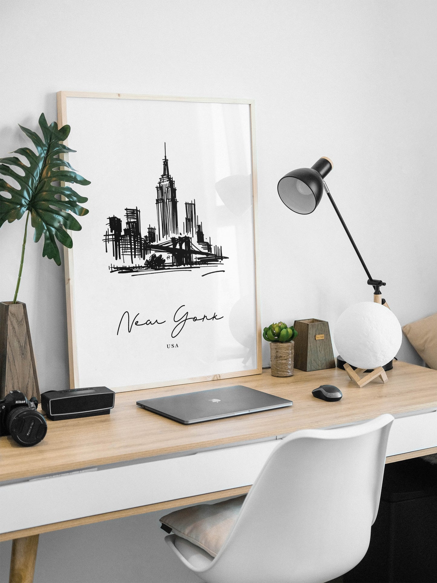 Poster paysage New York en cadre bois clair posé sur un bureau, lampe noire et ordinateur portable