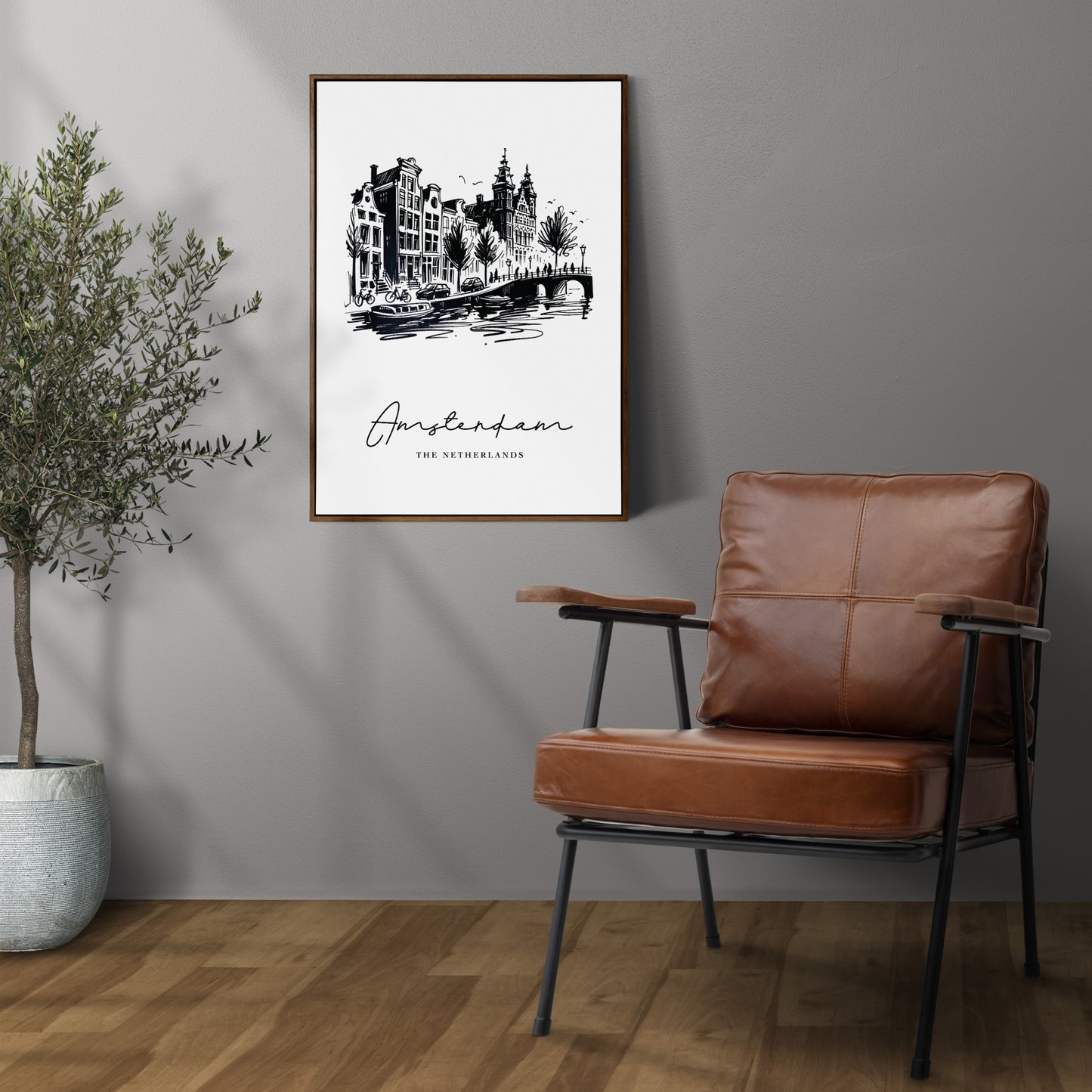 Poster des canaux d'Amsterdam en cadre bois foncé sur un mur gris, à côté d'un fauteuil en cuir et d'un olivier