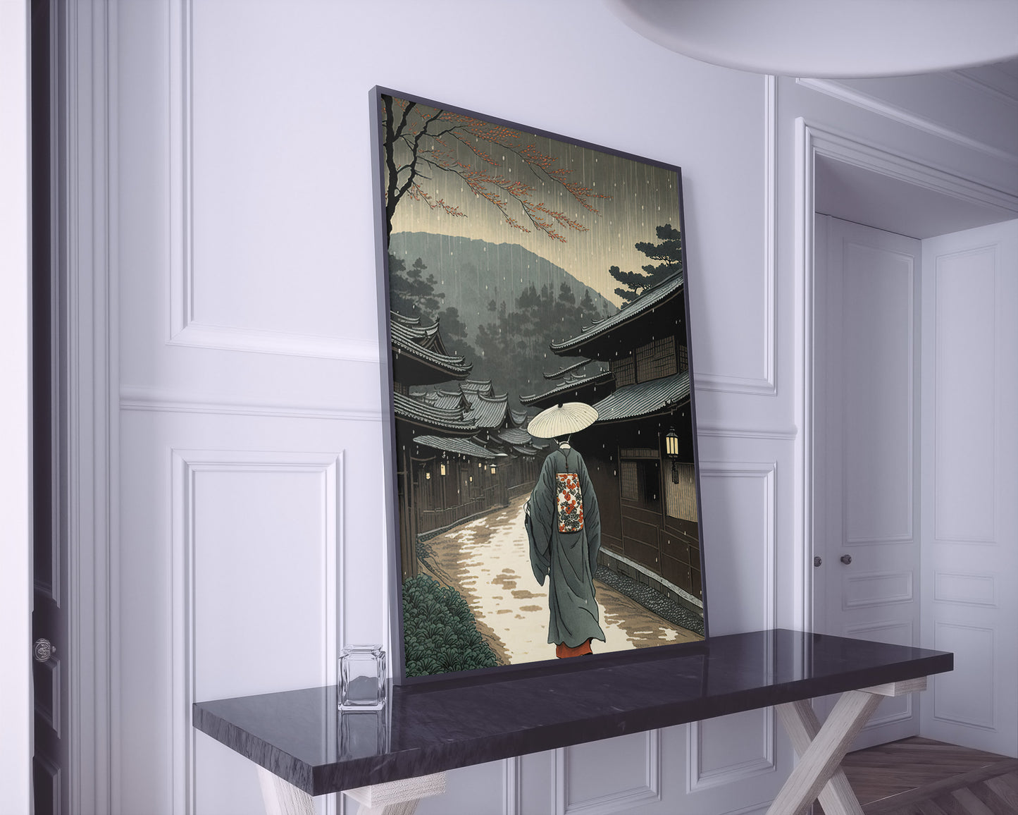 Poster village japonais en cadre noir posé sur une console en marbre noir, murs blancs à moulures