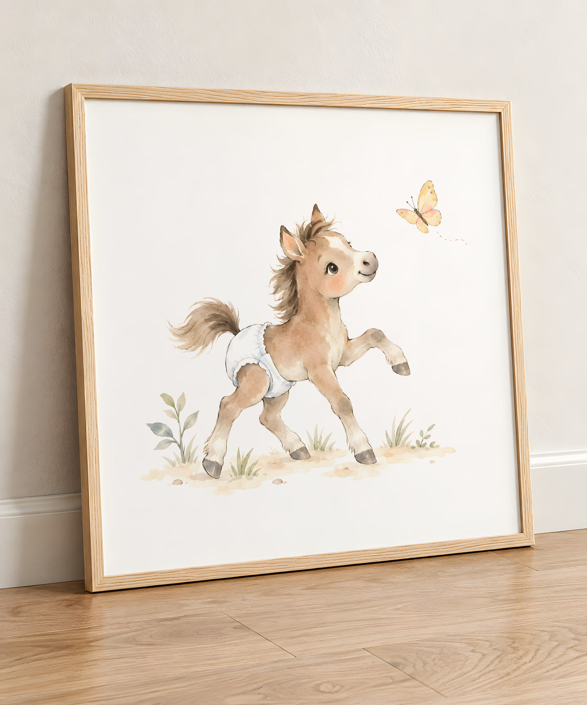 Un poulain en couche blanche poursuit un papillon dans le pré : cadre bois clair, 50 × 50 cm, en situation