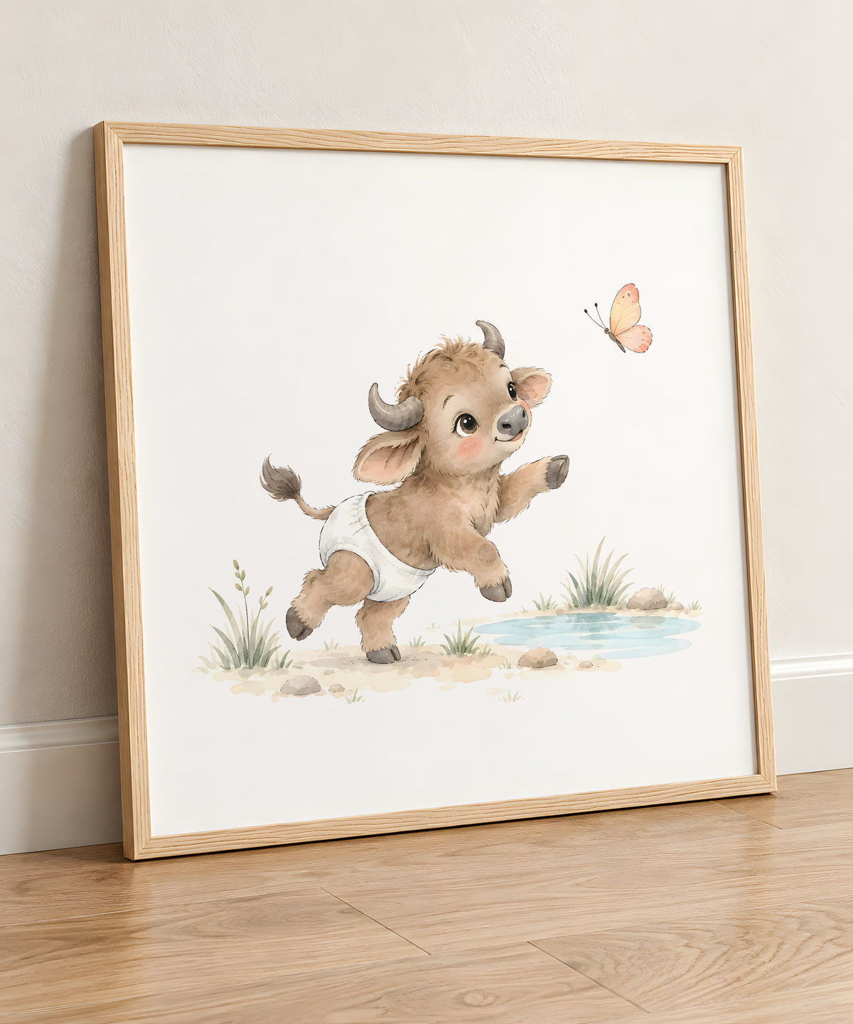 Bébé buffle en couche blanche tend les pattes vers un papillon : cadre bois clair, 50 × 50 cm, en situation