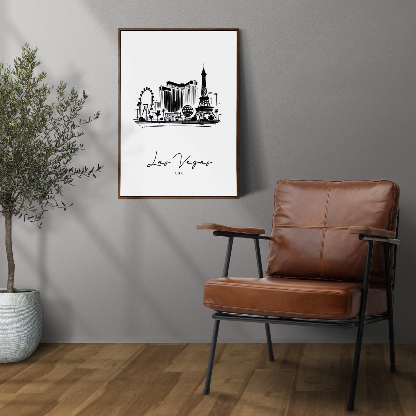 Poster des monuments de Las Vegas en cadre bois foncé sur un mur gris, à côté d'un fauteuil en cuir et d'un olivier