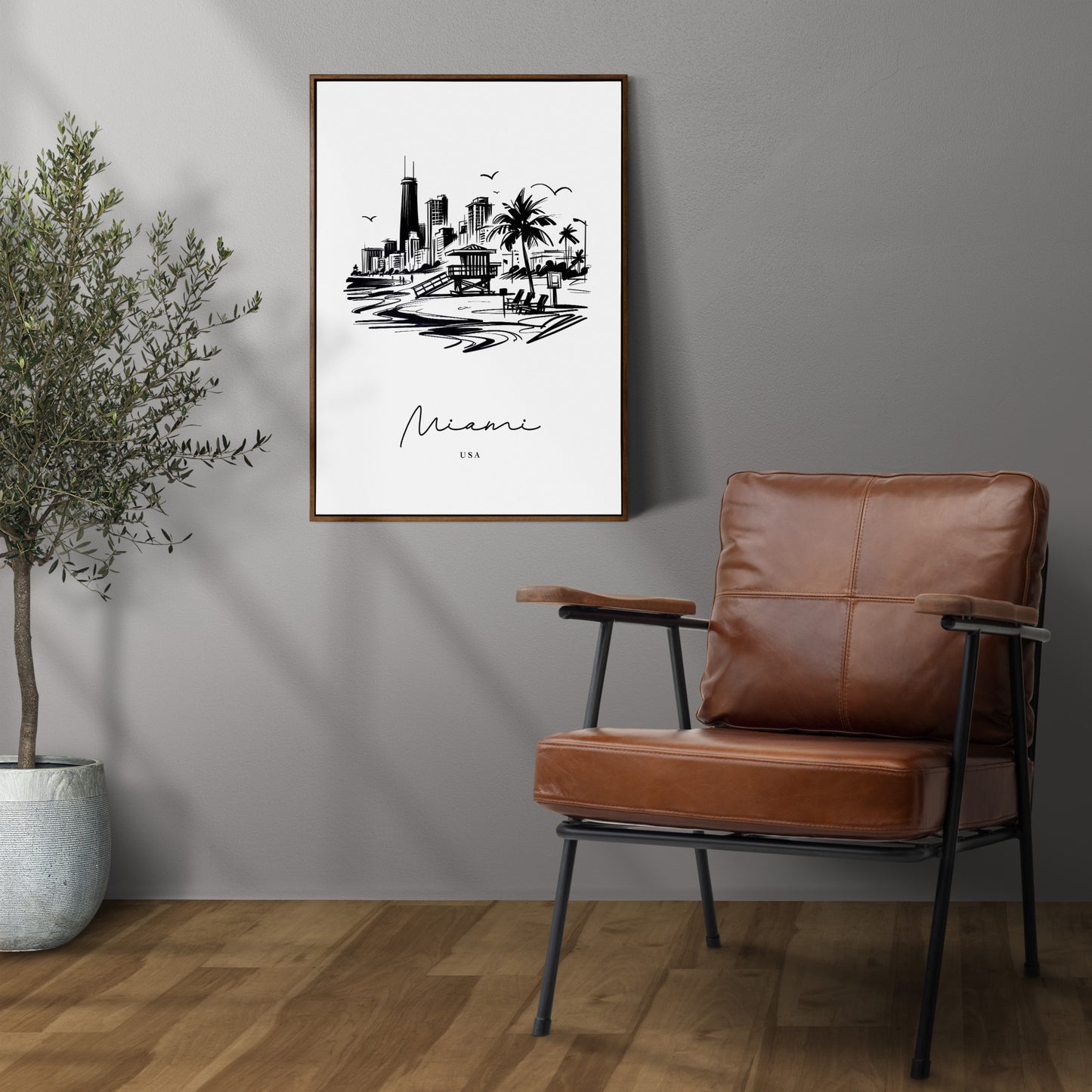 Affiche Miami noir et blanc au mur gris, cadre bois foncé au-dessus d'un fauteuil en cuir, olivier en pot