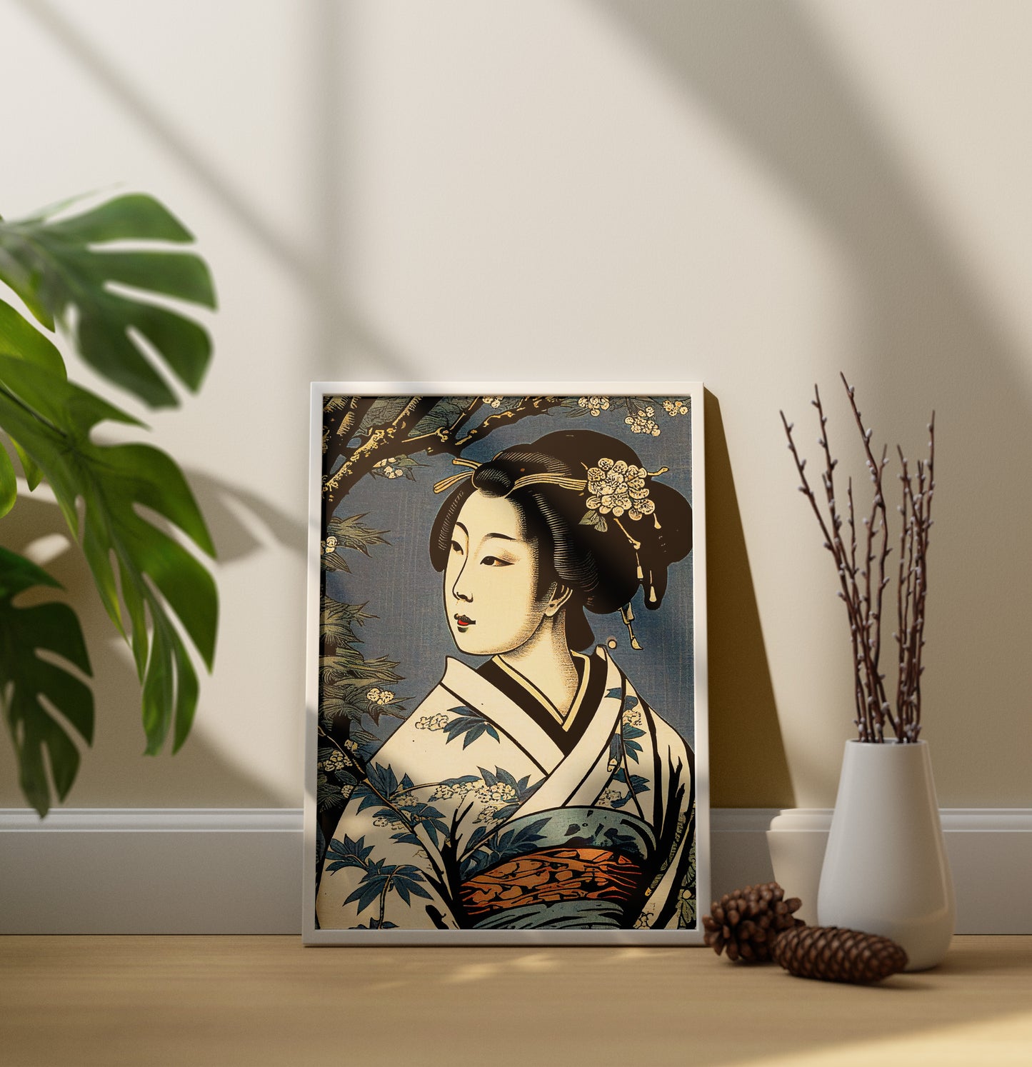 Poster geisha, cadre blanc, posé au sol près d'un vase de branches et d'une pomme de pin
