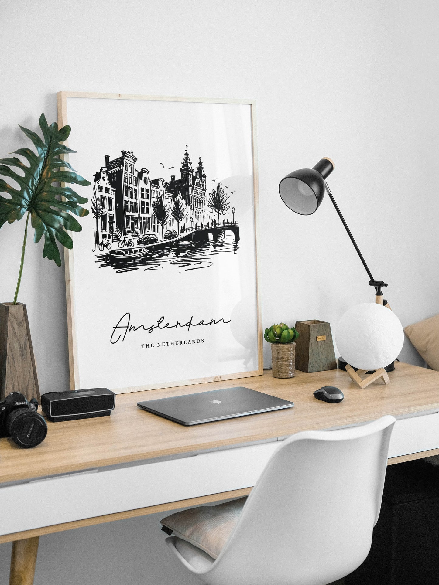 Poster des canaux d'Amsterdam en cadre bois clair posé sur un bureau, lampe noire et ordinateur portable
