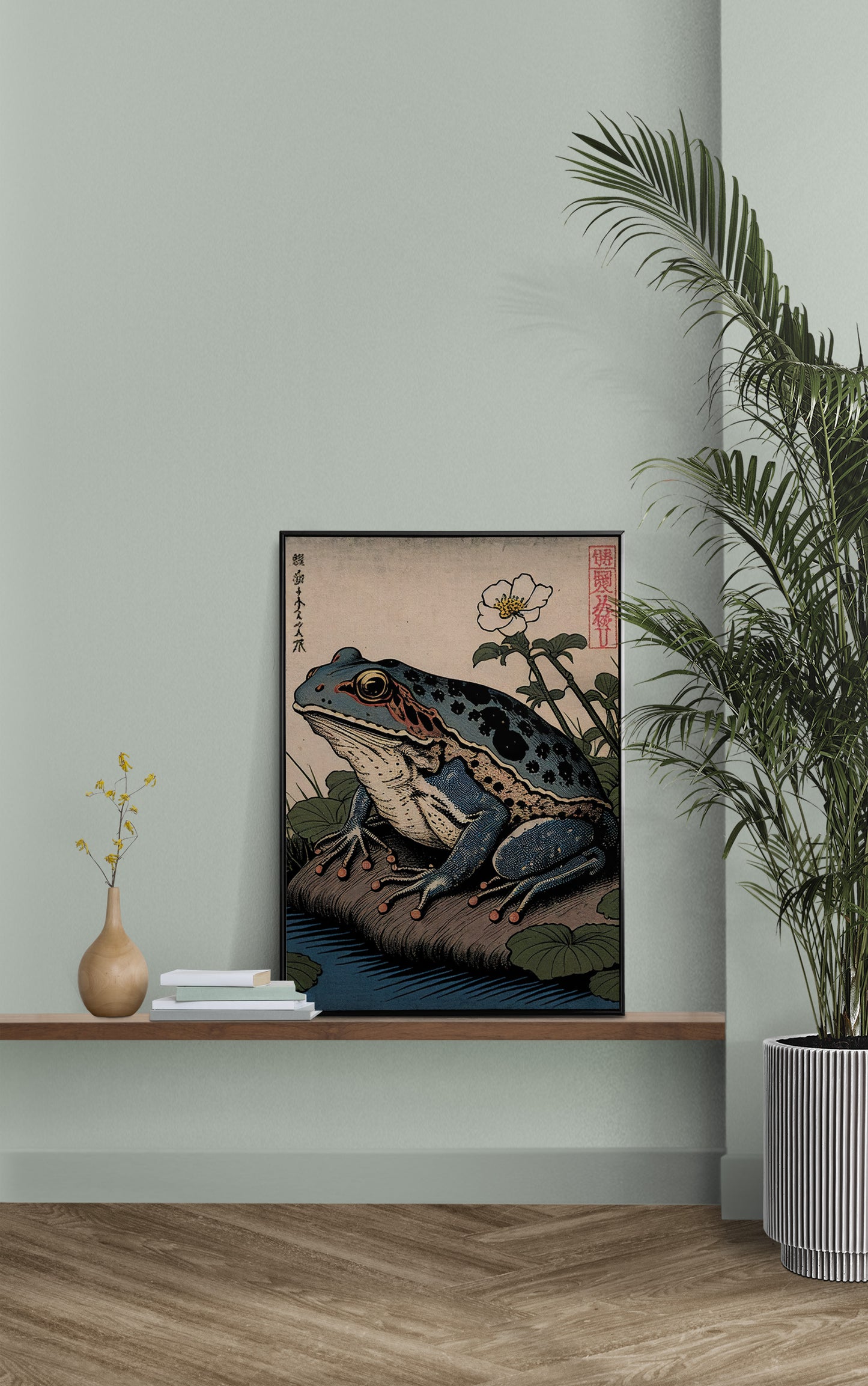 Poster grenouille art japonais posé sur une étagère murale, mur vert sauge et palmier en pot