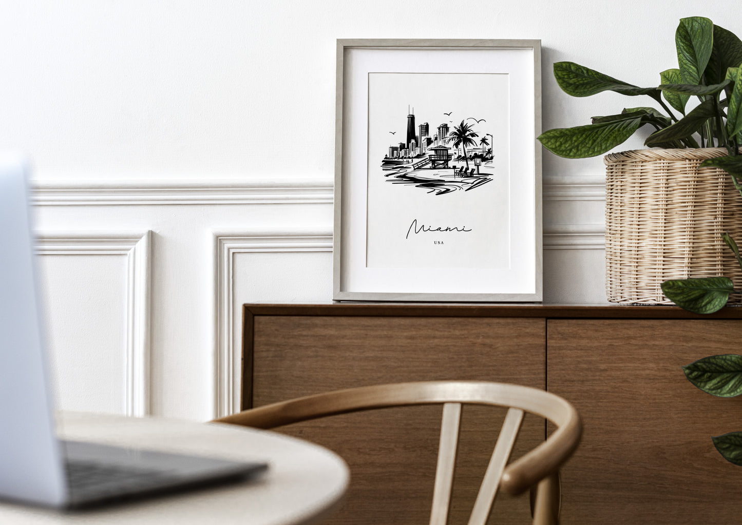 Affiche Miami noir et blanc, cadre bois clair et passe-partout sur une commode, plante verte et chaise en bois