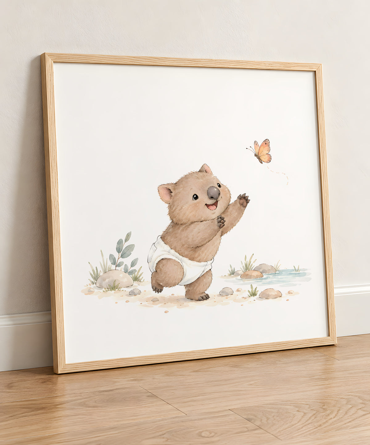 Aquarelle d'un bébé wombat en couche tendant la patte vers un papillon orange, affiche en cadre bois clair posée au sol