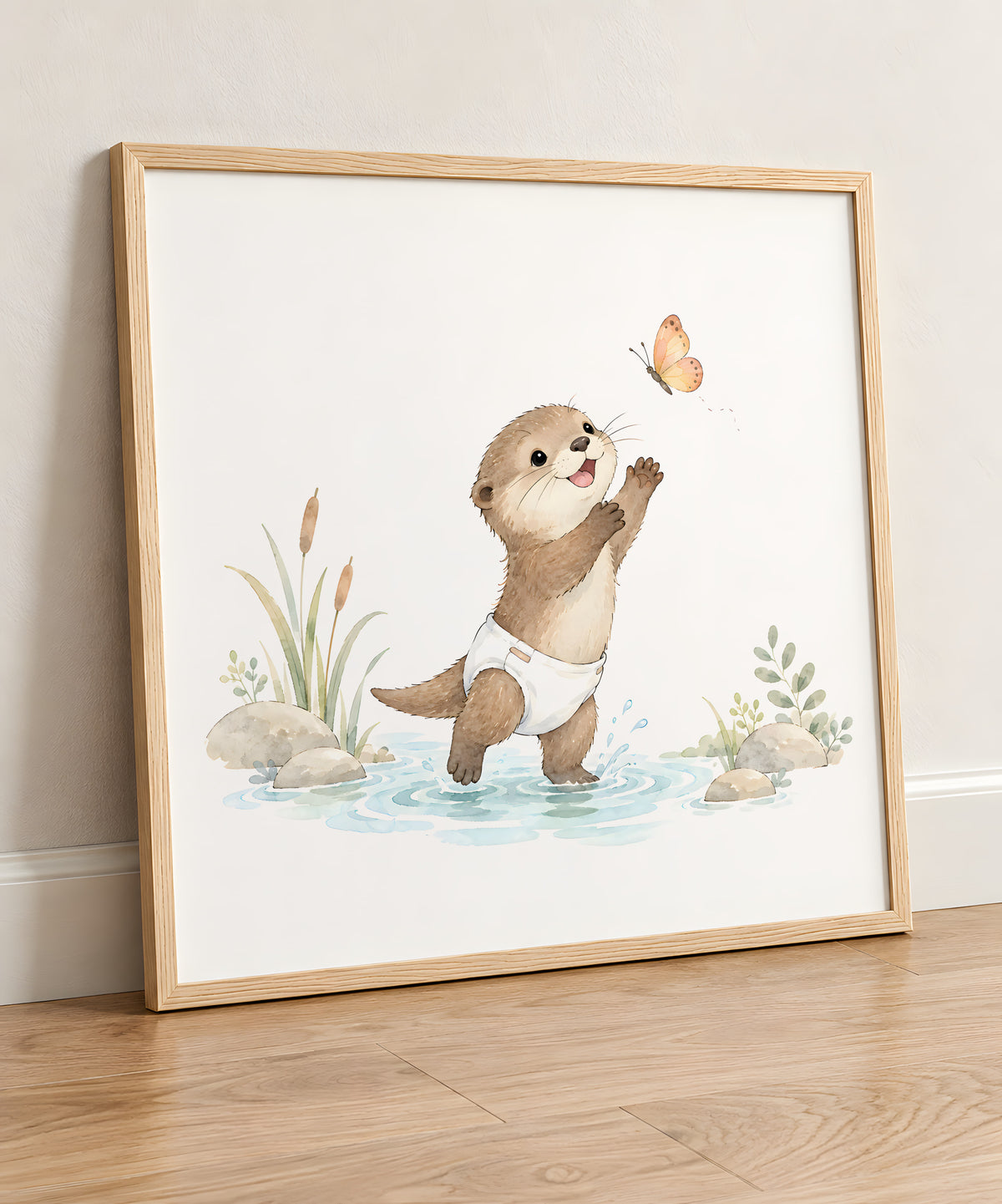 Bébé loutre tente d’attraper un papillon au bord de l’eau : cadre bois clair, 50 × 50 cm, en situation