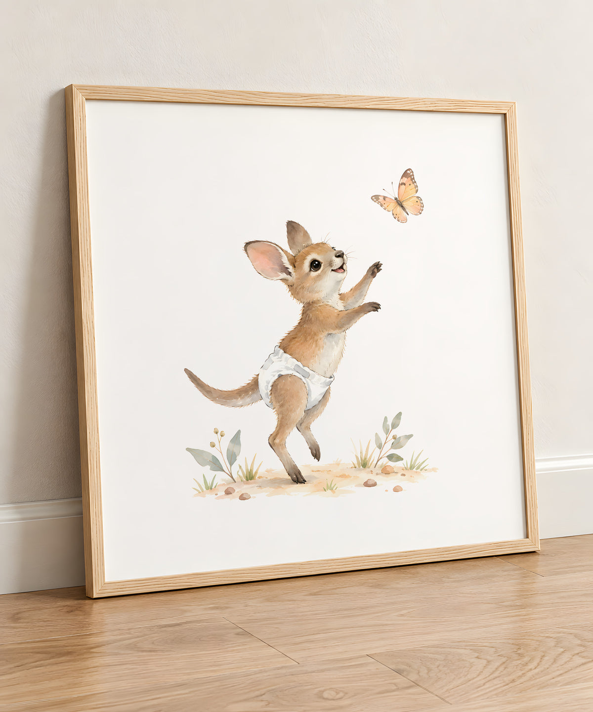 Bébé wallaby en couche blanche tend les pattes vers un papillon : cadre bois clair, 50 × 50 cm, en situation