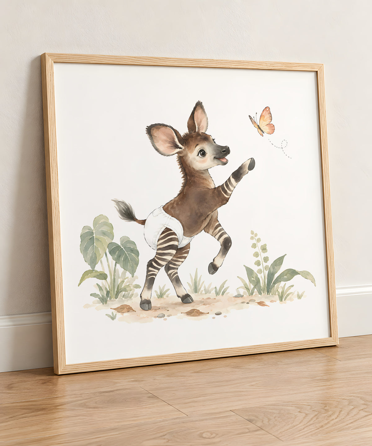 Bébé okapi en couche blanche tend le sabot vers un papillon : cadre bois clair, 50 × 50 cm, en situation